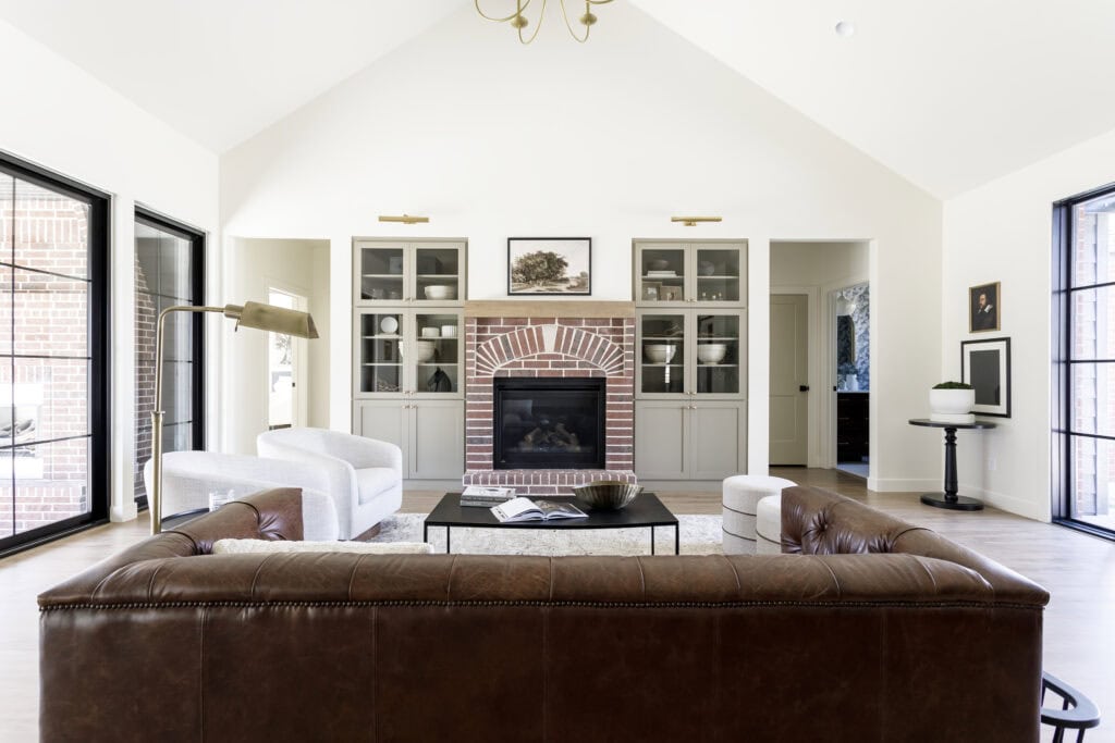 red brick fireplace, brown leather sofa, black metal coffee table, built-ins and intentional layered lighting 