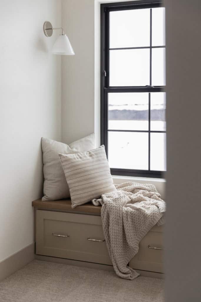 a classic example of a Cozy Corner Wall Sconce, a comfortable builtin bench with two pillows by the window in a custom home by Meg & co Twin Falls Idaho
