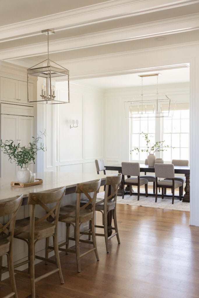 a view into a beautiful dining room design with a statement cage linear chandelier and wainscoting panels 