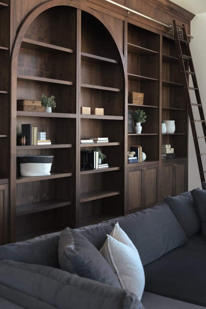 a close-up photo of built-ins in dark walnut in a custom office by Meg & Co, open shelving, the middle part is arched and there is a tall sliding library step ladder on the right 