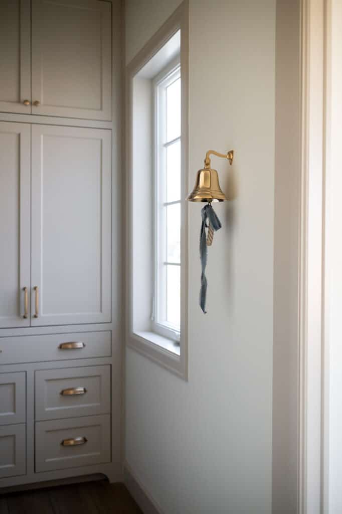a photo of custom cabinetry in a mudroom with an aged brass wall bell in a custom home by Meg & Co