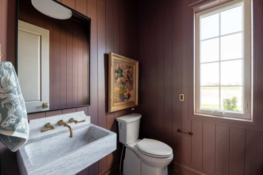 a large art that depicts vibrant flowers in a vase, displayed in the custom bathroom by Meg & Co  bathroom is painted in Bateau Brown that pairs beautifully with gold fixtures and a gold frame