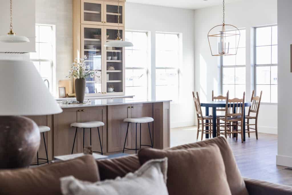 Bright, modern kitchen and dining area with wooden cabinets, white countertops, three barstools and Glass Cabinetry as a Beautiful Design Moment