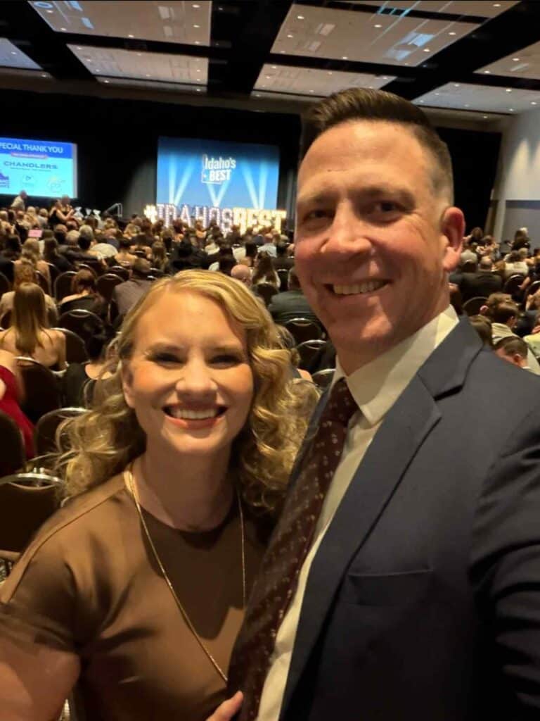 Two attendees smile for a photo inside the 2026 Idaho’s Best Awards ceremony with the event stage and audience behind them.