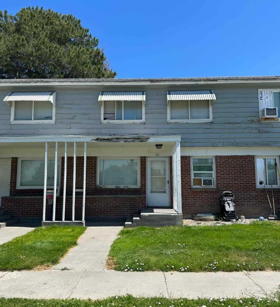 Exterior of a two-story residential building with brick and weathered siding before renovation work.