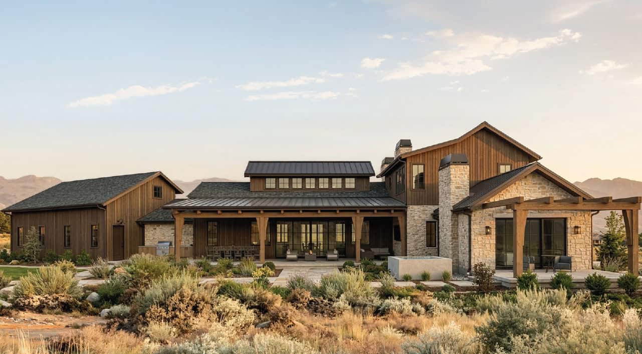 Rear exterior rendering of The Merrick in Hailey, Idaho, featuring natural stone, dark wood siding, timber-framed outdoor living areas, and mountain views.