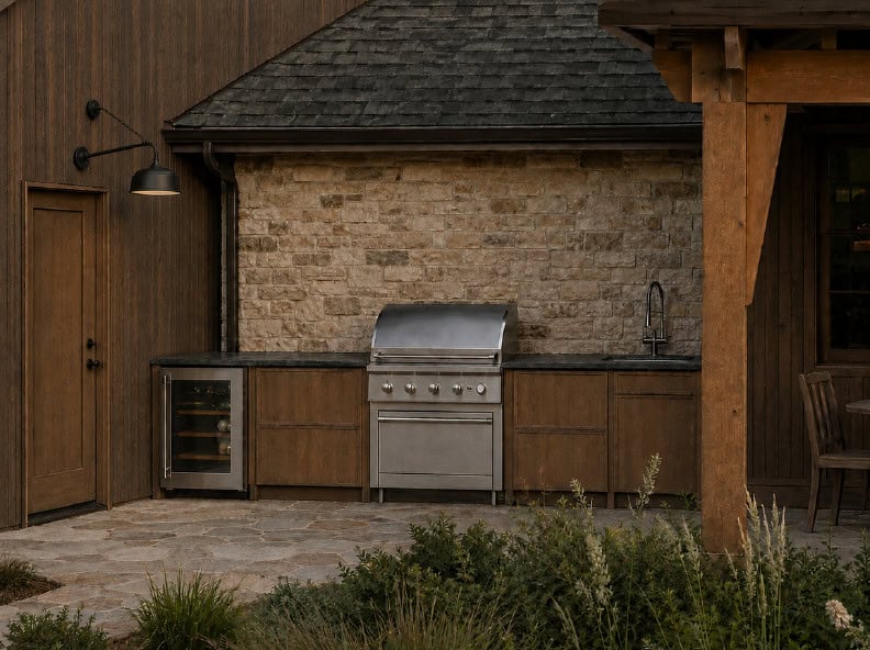 Outdoor Kitchen - Custom Home Hailey Idaho Covered outdoor kitchen at The Merrick featuring natural stone, wood cabinetry, built-in grill, beverage refrigerator, and mountain modern finishes.